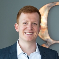 Portraitfoto von einem lachenden Mann mit roten kurzen Haaren, weißem Hemd und dunklem Jacket.