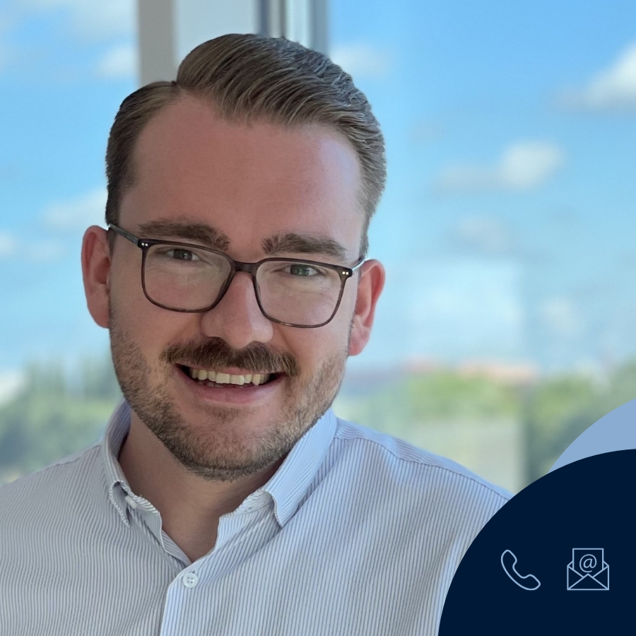 Vertriebsmitarbeiter Keno Rademaker trägt ein hellblau-weiß gestreiftes Hemd, steht vor einem Fenster mit Blick auf die Weser vor einem unscharfem Hintergrund.